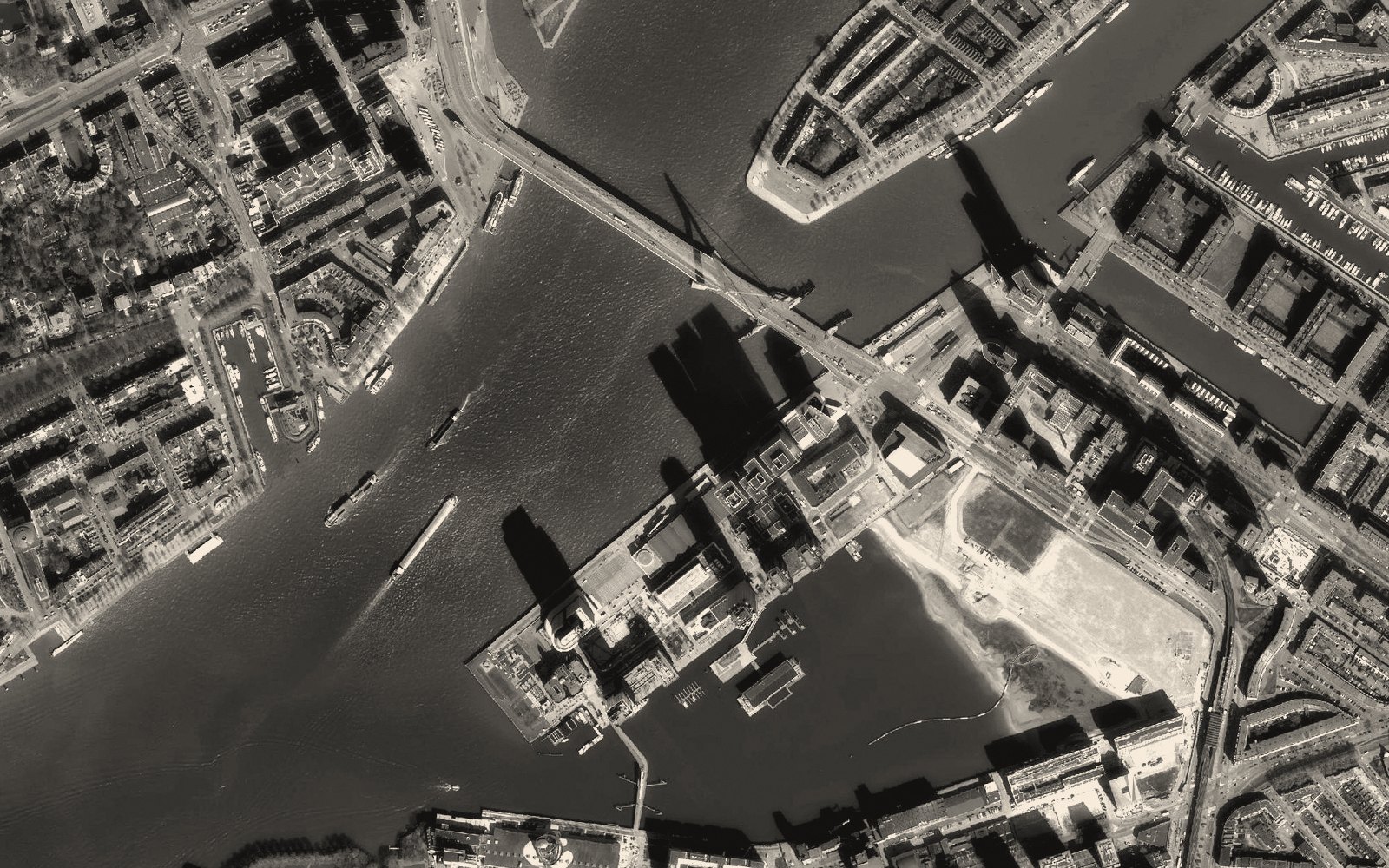 Aerial view of a river through a port city, vessels underway leaving wakes