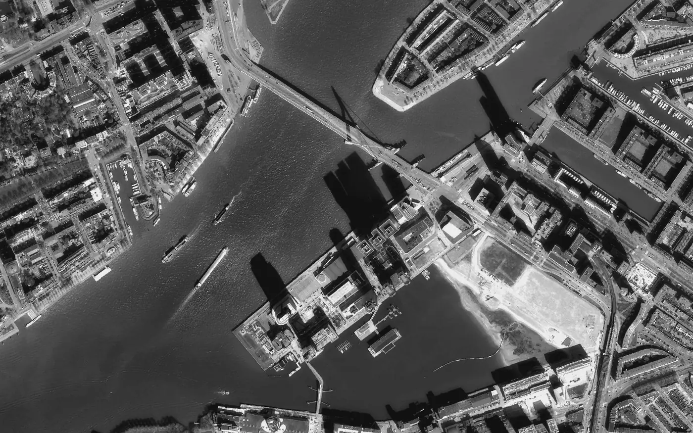 Aerial view of a river through a port city, vessels underway leaving wakes
